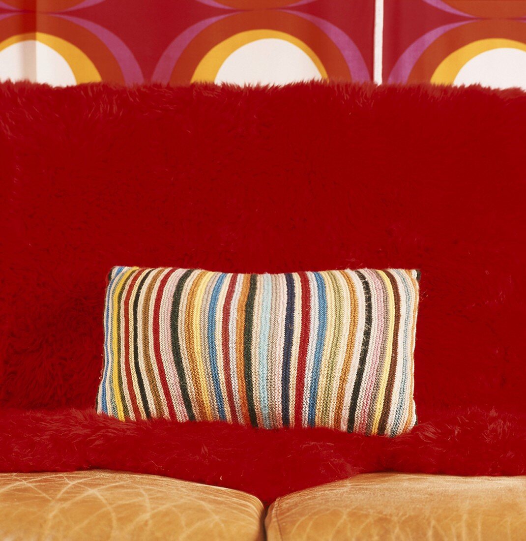 Kissen mit gestreiftem Häkelbezug auf roter Couch vor Tapete im siebziger Jahre Stil