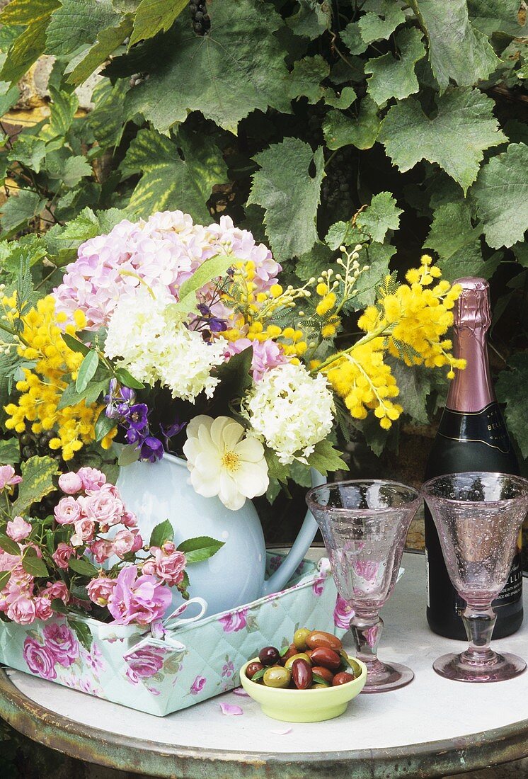 Bunter Blumenstraus mit Sekt und Gläsern auf Gartentisch