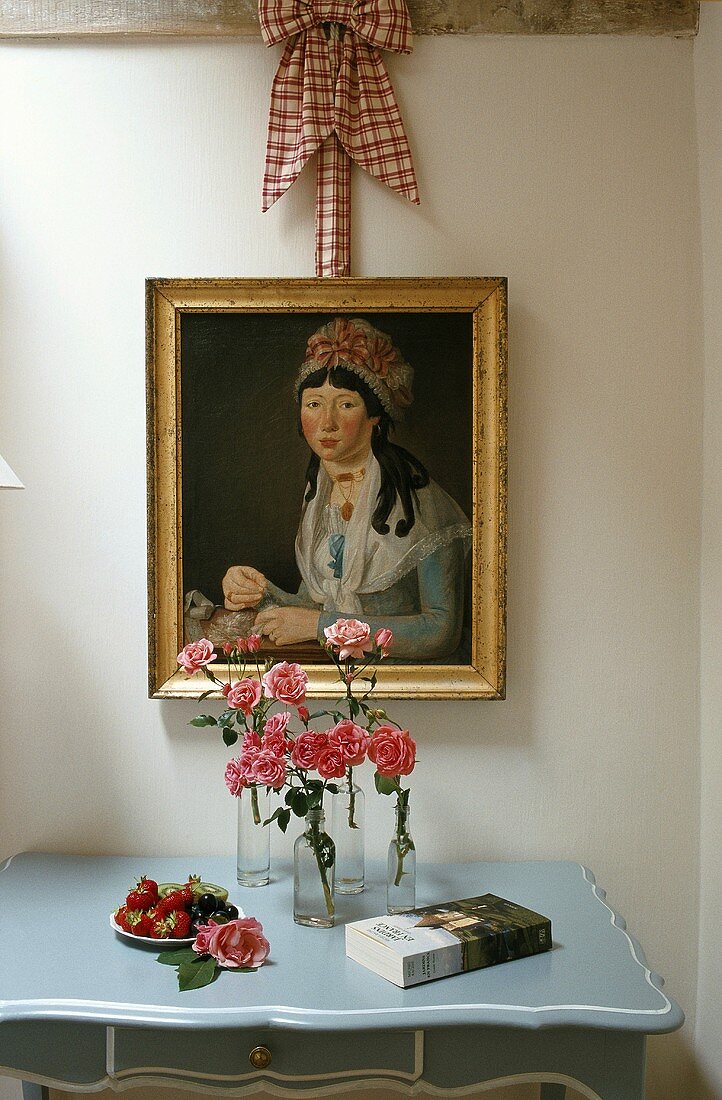 Zimmerausschnitt mit antikem Gemälde über Wandtischchen mit Rosen in Blumenvasen