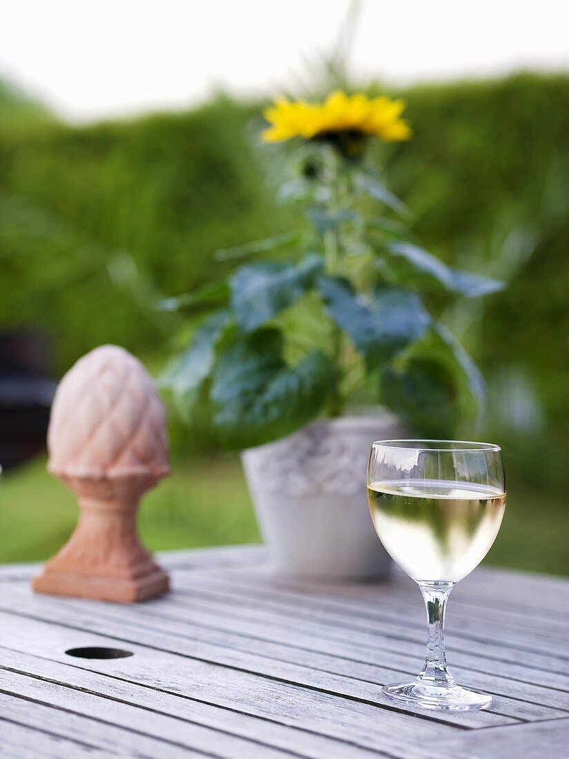 Weissweinglas, Sonnenblume und Terracottafigur auf Gartentisch