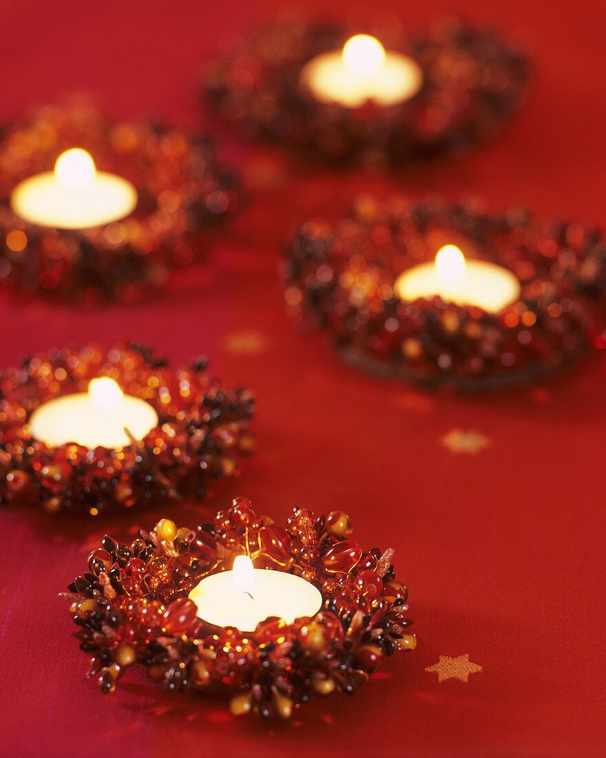 Fünf Teelichte in Perlen-Kränzen auf rotem Tischtuch