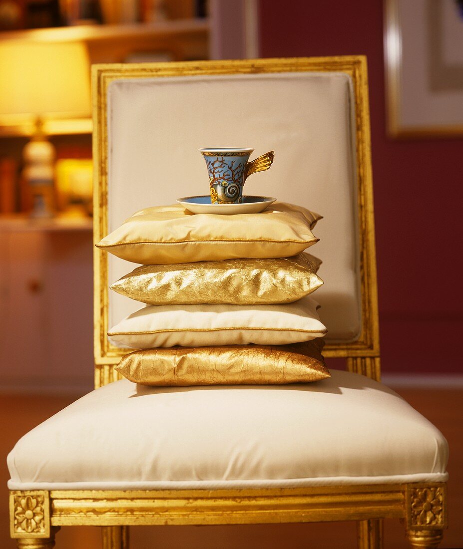 Stack of cushions and designer coffee cup and saucer on chair