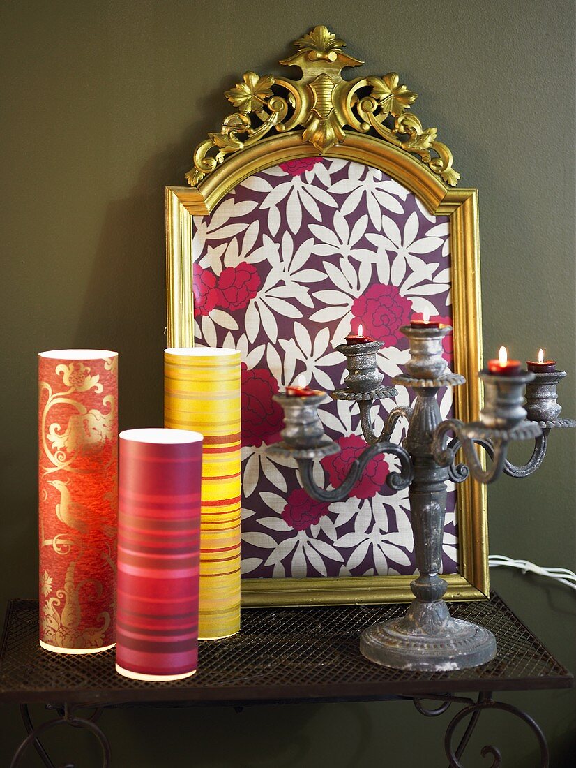 Colorful wrapping paper and antique candelabra in front of a gold frame containing a patterned paper