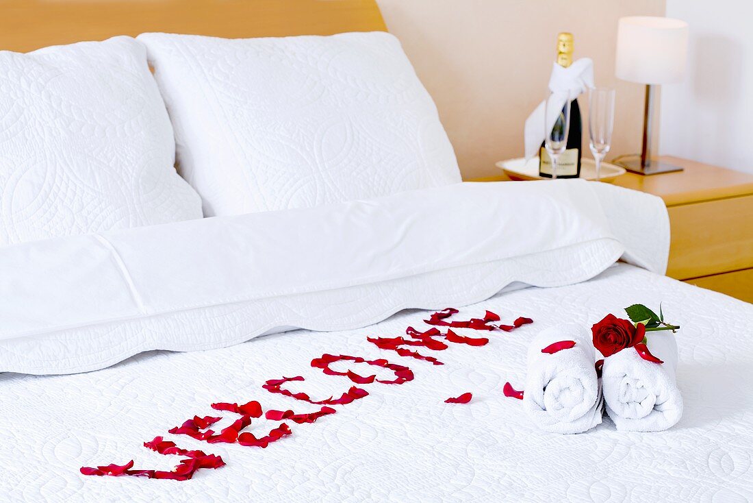 Red roses, handtowels and the word 'Welcome' written on a bed in a hotel room