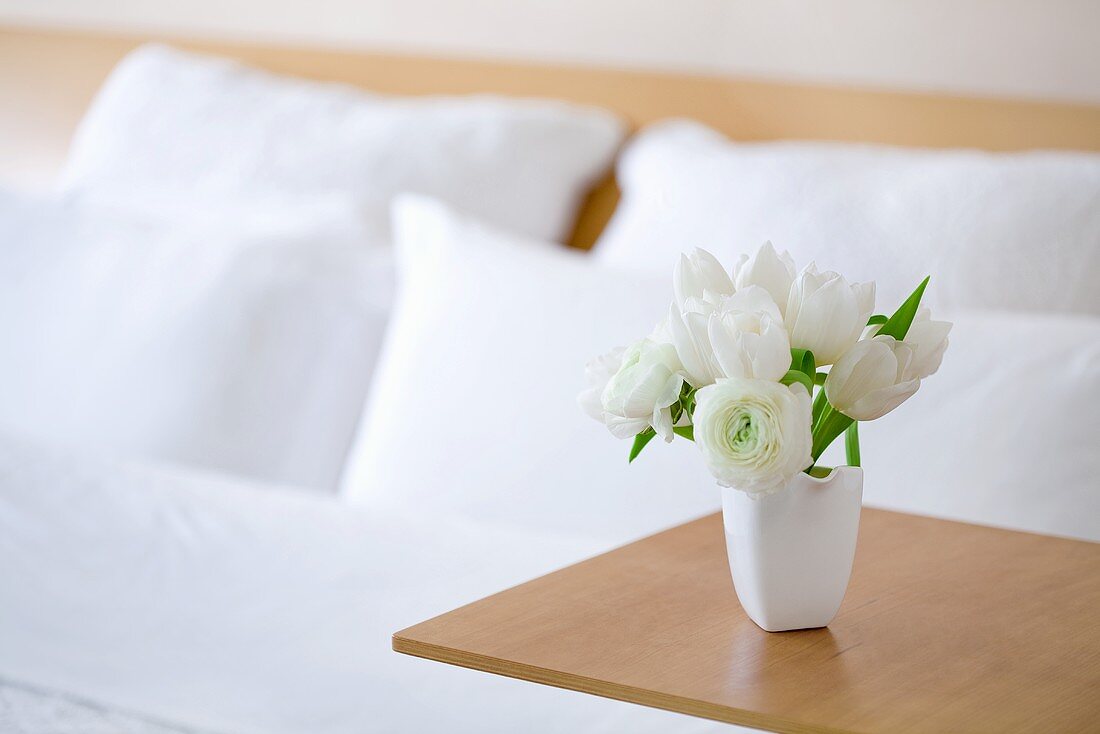 Weißer Tulpenstrauß auf Beistelltisch eines Doppelbettes