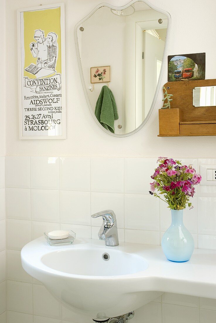 A vase of flowers on a wash basin and a mirror on a white-tiled wall