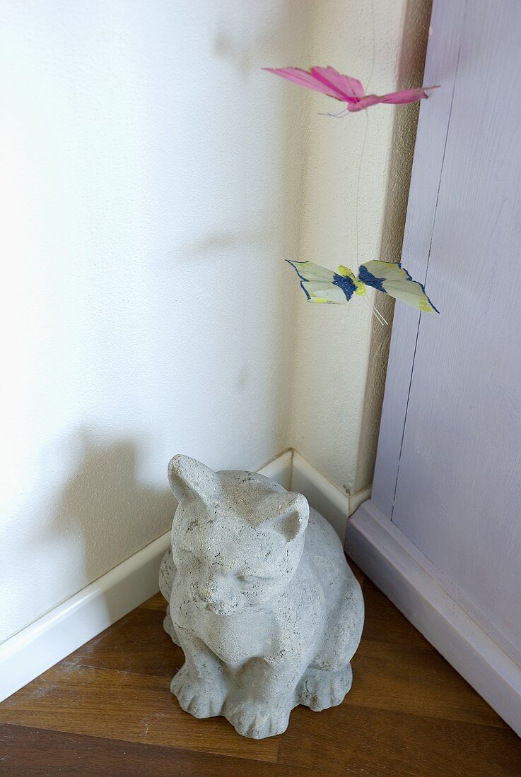Tierfigur aus Stein und Papierschmetterlinge in Zimmerecke
