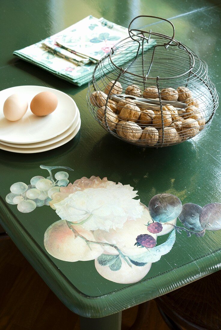 Nüsse im Drahtkorb und Eier auf Unterteller auf bemaltem Tisch