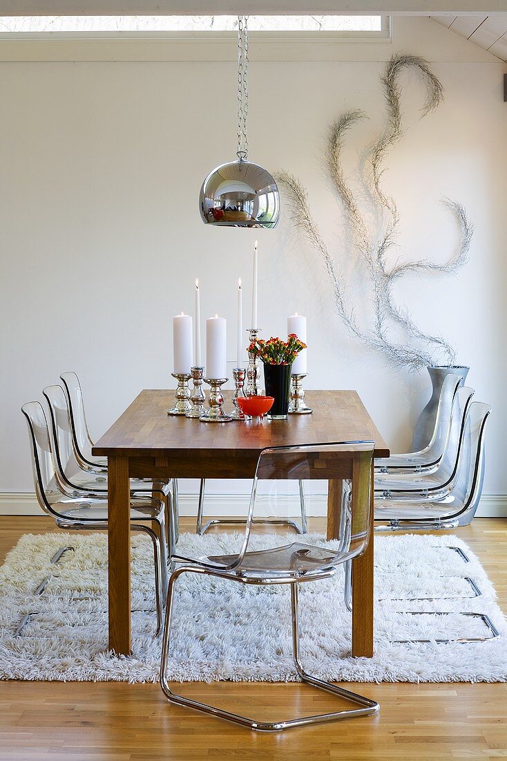 Wohnraum mit Esstisch aus Holz, Freischwinger Stühlen aus Plexiglas, silberner Hängeleuchte & Flokati-Teppich
