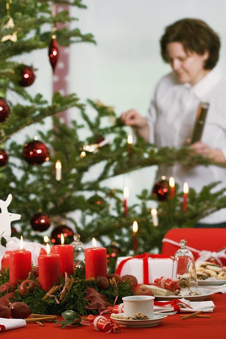 A Christmassy table, with a woman lighting a candle on the Christmas tree