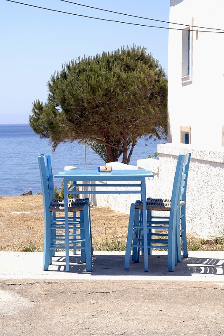 Blauer Tisch mit Stühlen, im Hintergrund das Meer