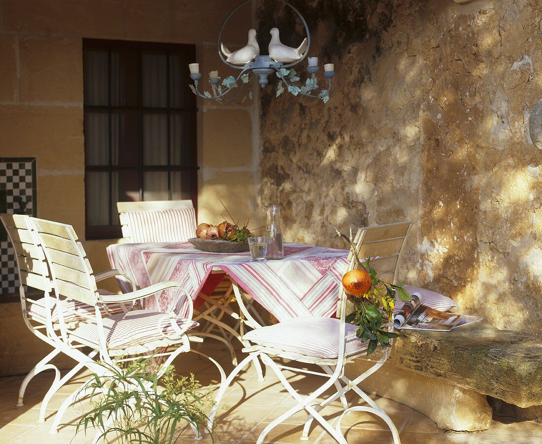 Steinbank & Tisch mit Gartenstühlen auf sommerlicher Veranda