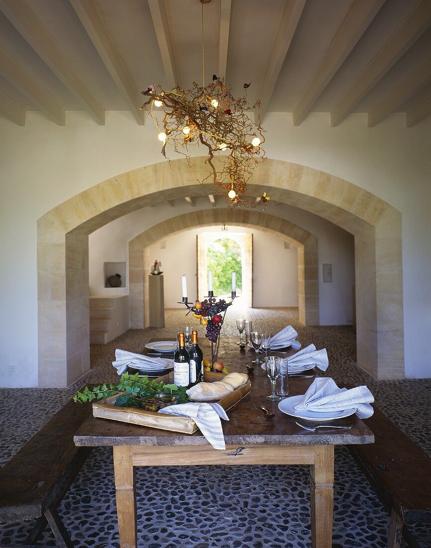 Gedeckter Esstisch mit Holzbänken in Wohnraum mit Mosaikfliesenboden & Rundbogen-Durchgang