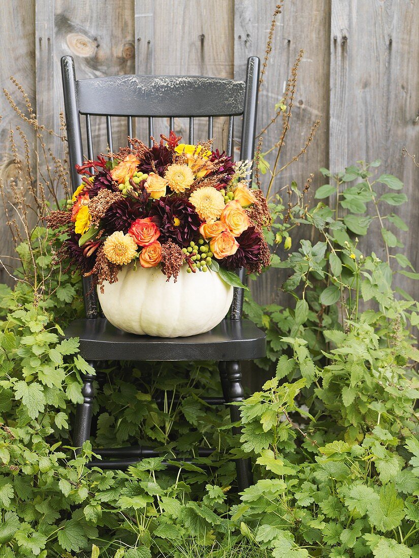 Autumn flowers in hollowed-out pumpkin on a garden chair