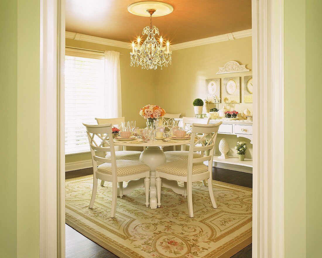 Blick in Esszimmer mit festlich gedecktem, rundem Tisch, Kronleuchter & Teppich