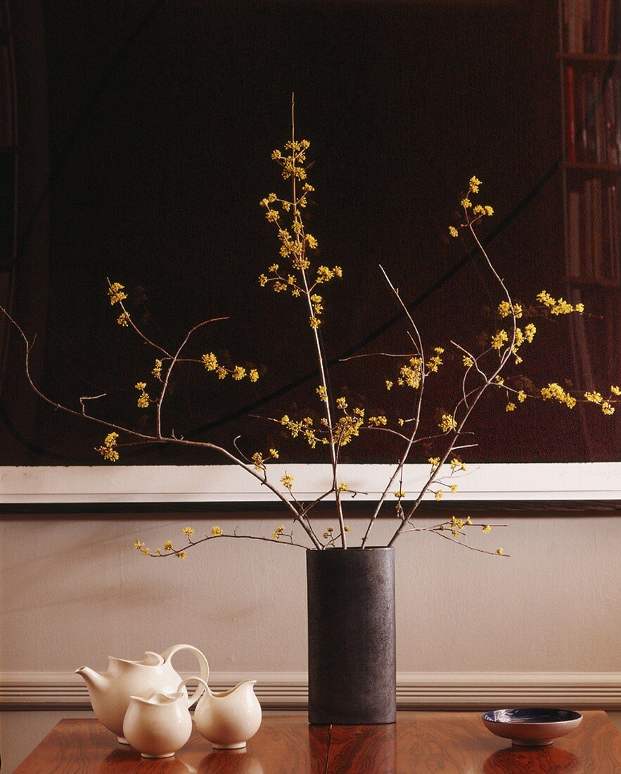 Vase mit Zweigen und Teegeschirr auf einem Tisch