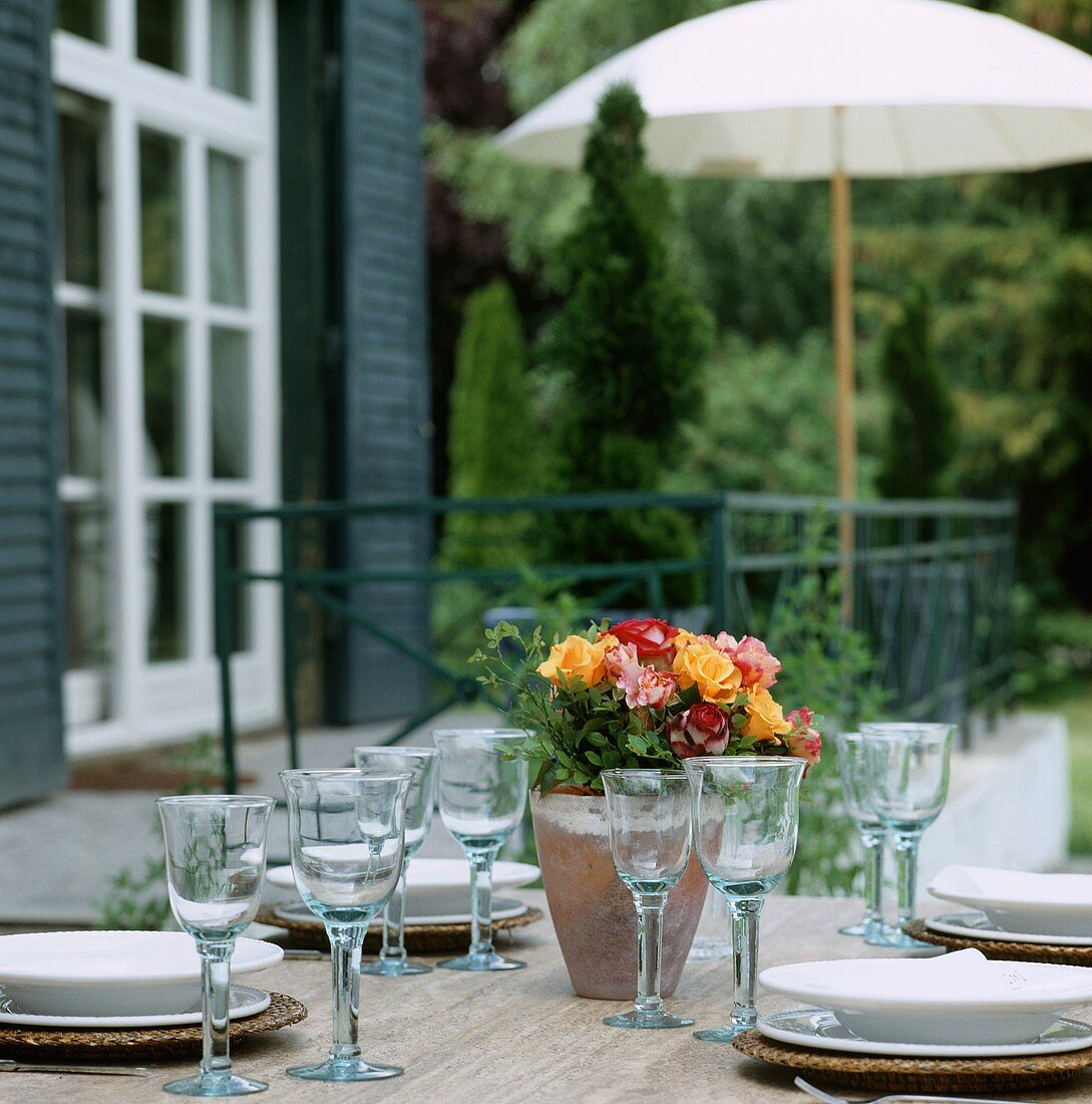 Gedeckter Tisch mit Rosenstrauss auf Terrasse im Garten