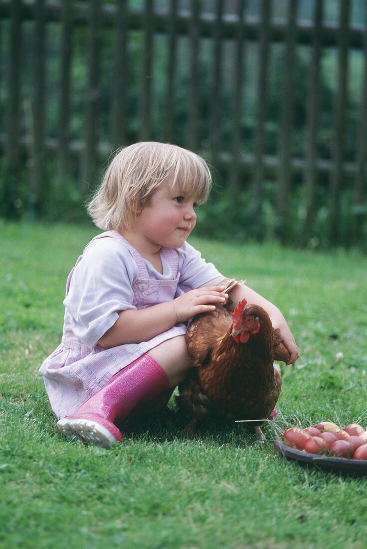 A little girl sitting on the grass with a chicken