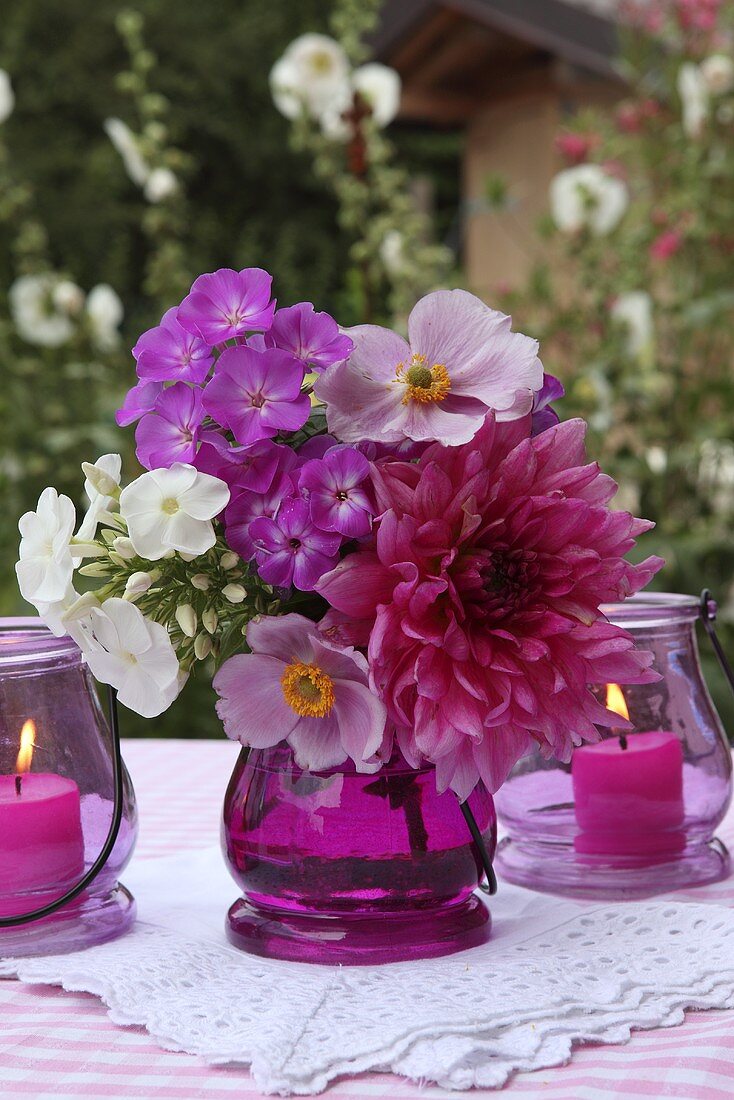 Pinkfarbener Blumenstrauss und Windlichter auf Gartentisch