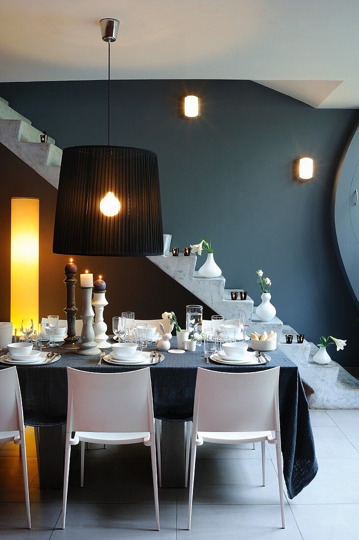 Esszimmer mit gedecktem Tisch, schwarzer Hängeleuchte & geländerlosem Treppenaufgang im Hintergrund