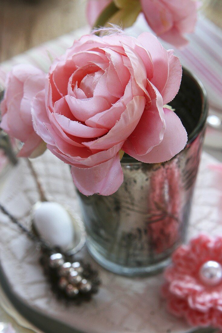 Rosafarbene Kunststoffrose und Häkelblume als Tischdeko