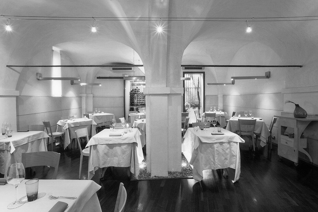 A black and white photo of a designer restaurant with a vaulted ceiling and halogen lights