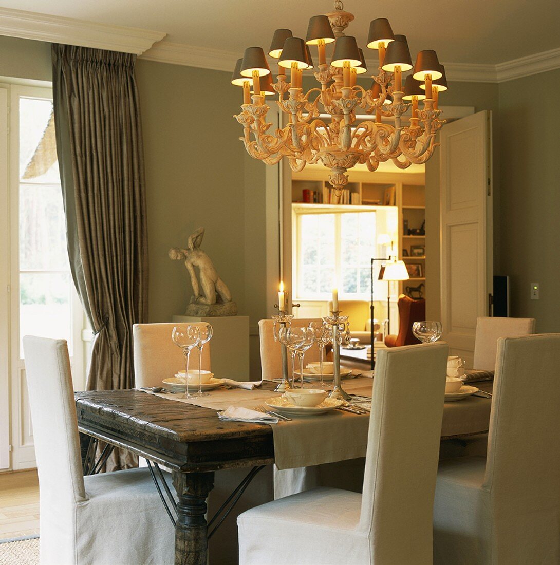 Esszimmer mit gedecktem Esstisch, Stühlen mit weissen Hussen & Kronleuchter mit Lampenschirmchen