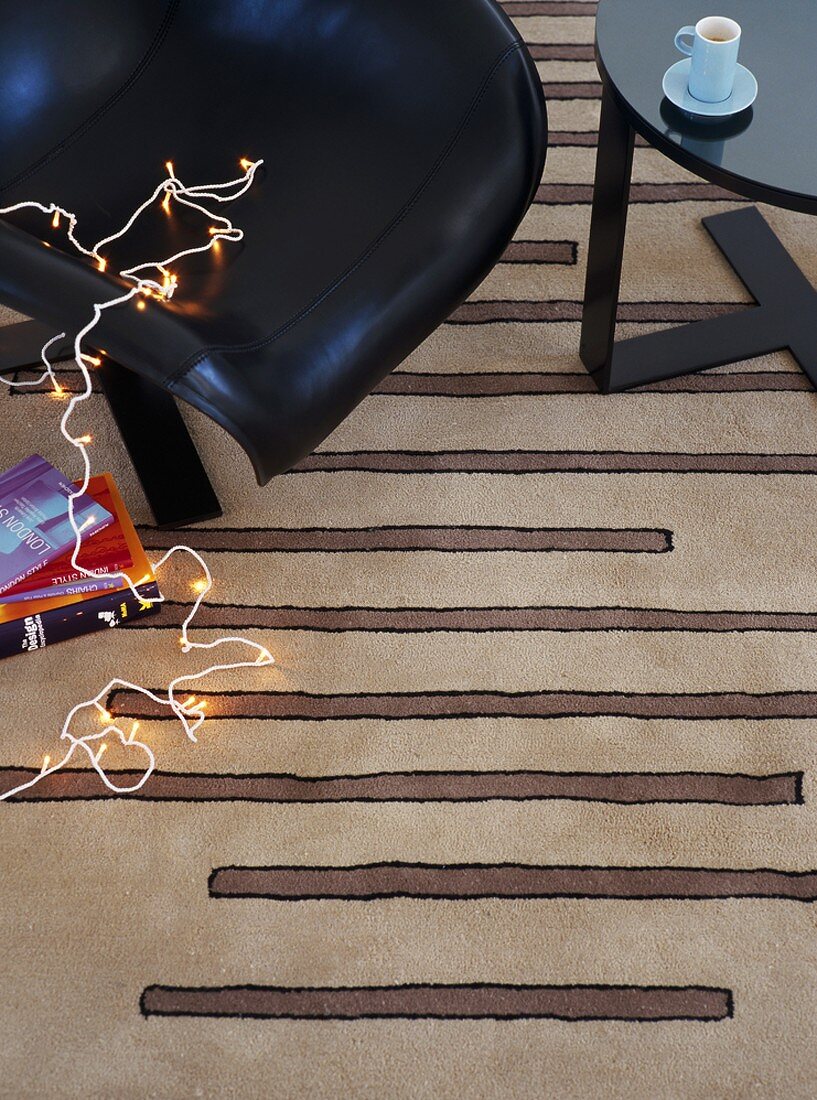 Lichterkette auf schwarzem Stuhl & beige-gestreiftem Teppich liegend (Ausschnitt)