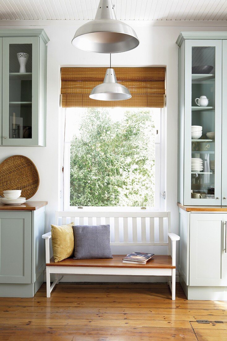 Kleine Holzsitzbank zwischen Küchenschränken unter Fenster mit Raffrollo