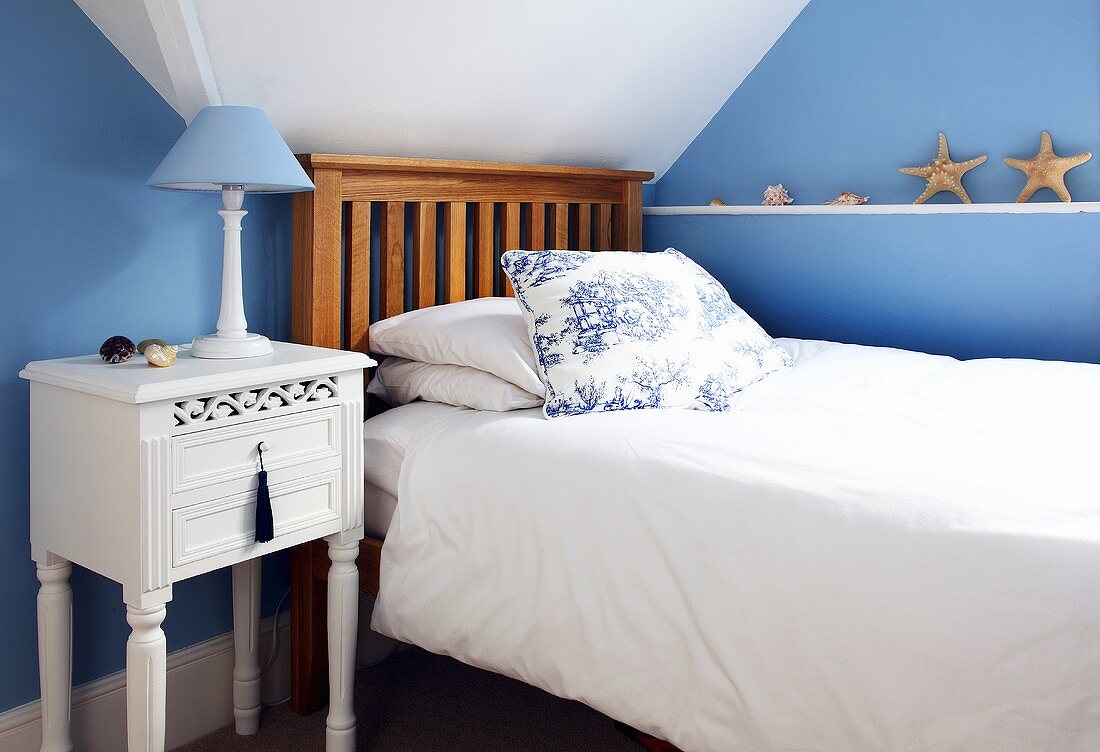 Schlafzimmer mit blauen Wänden, Bett, Nachttischchen, Tischlampe und maritimer Deko