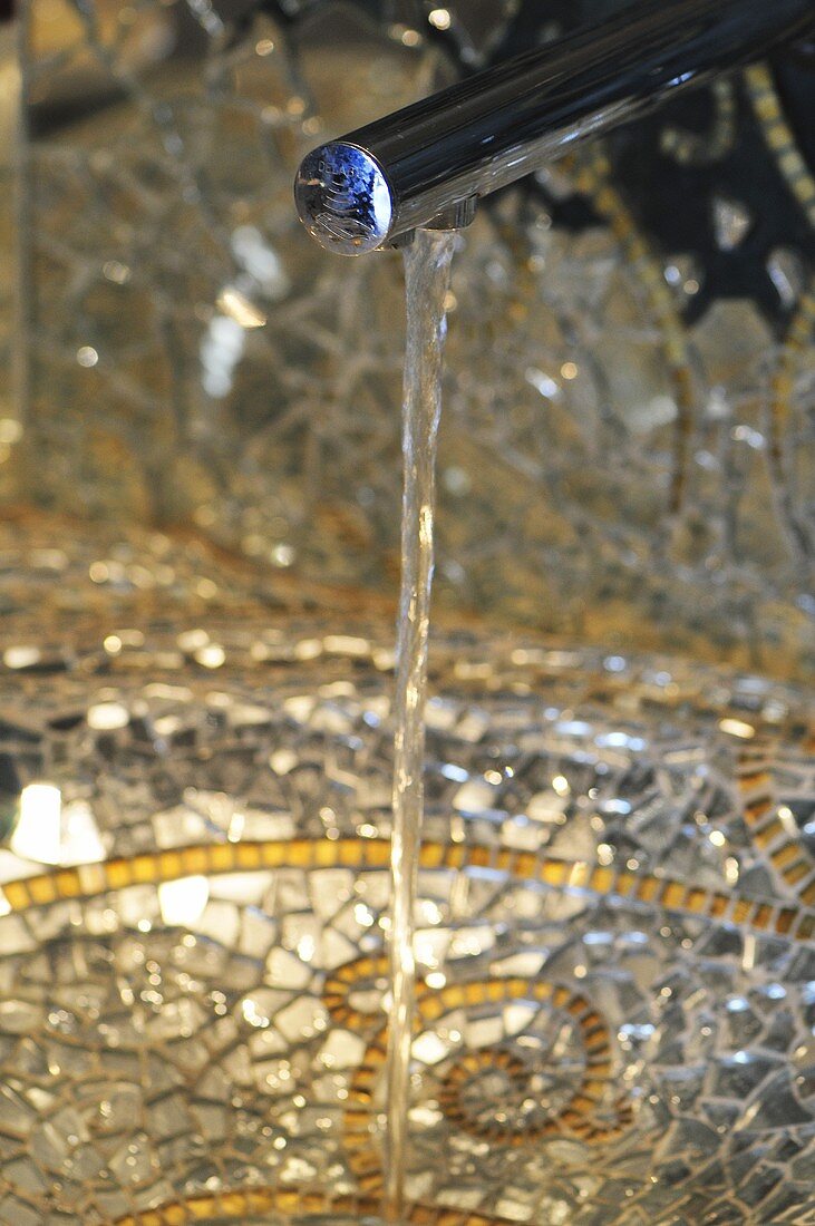 Wasser fliesst in ein mit Mosaiksteinen ausgelegtes Waschbecken