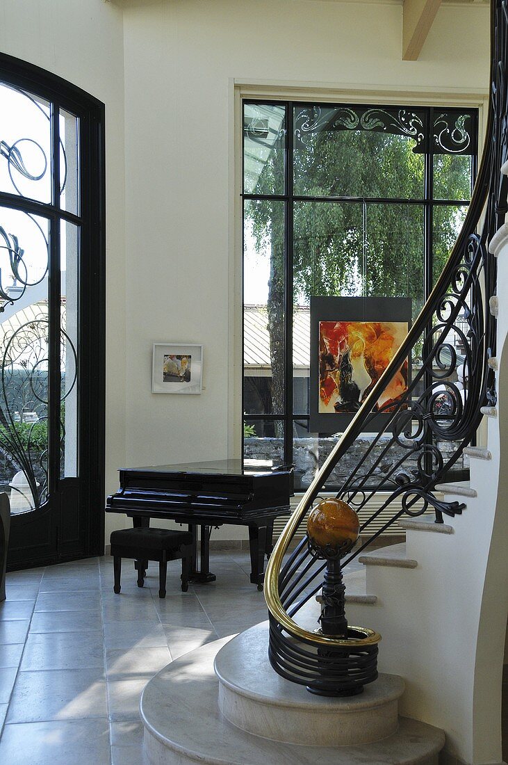 Wohnraum mit Klavier, raumhohen ornamentverzierten Fenstern & Treppenaufgang mit ornamentalem Geländer