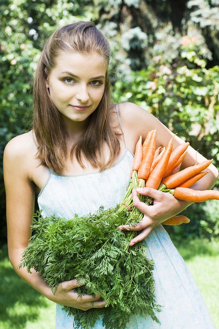 Woman holding fresh carrots in garden