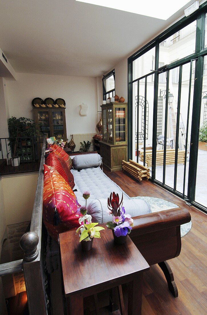 Wohnzimmer mit Sofa und Blick durch raumhohe Fenster auf Terrasse