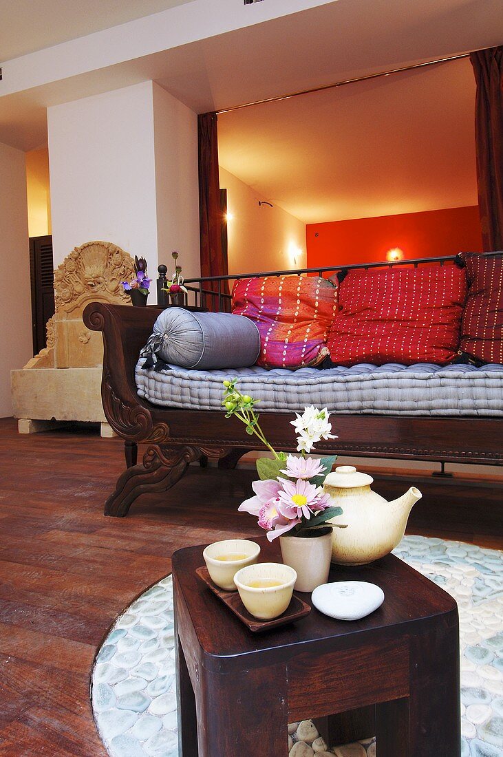 Wohnraum mit Holzsofa & Beistelltischchen mit Teegeschirr, Blumengesteck und Seife