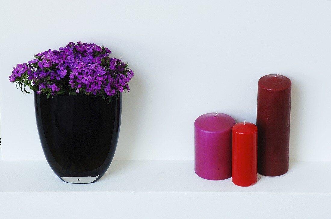 Vase mit lila Blumen und drei Kerzen