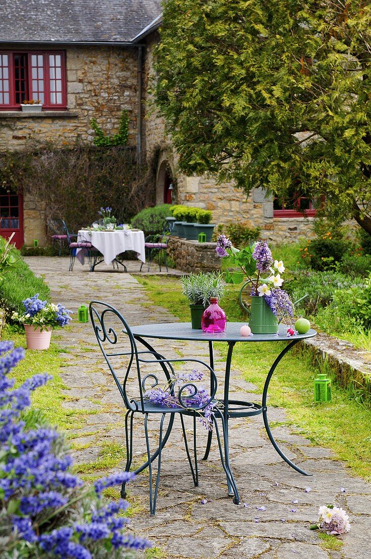 Gartenstuhl & Gartentisch mit Blumen auf gepflastertem Weg zum Haus