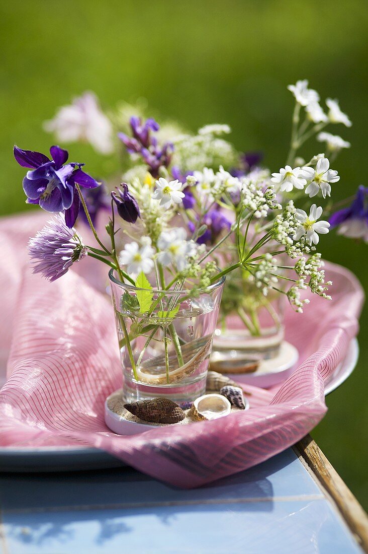 Blumenvase mit Wiesenblumen und Schneckenhäuser auf Tablett