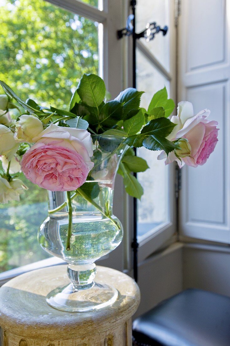Rosenstrauss in Glasvase auf Beistelltisch vor Fenster