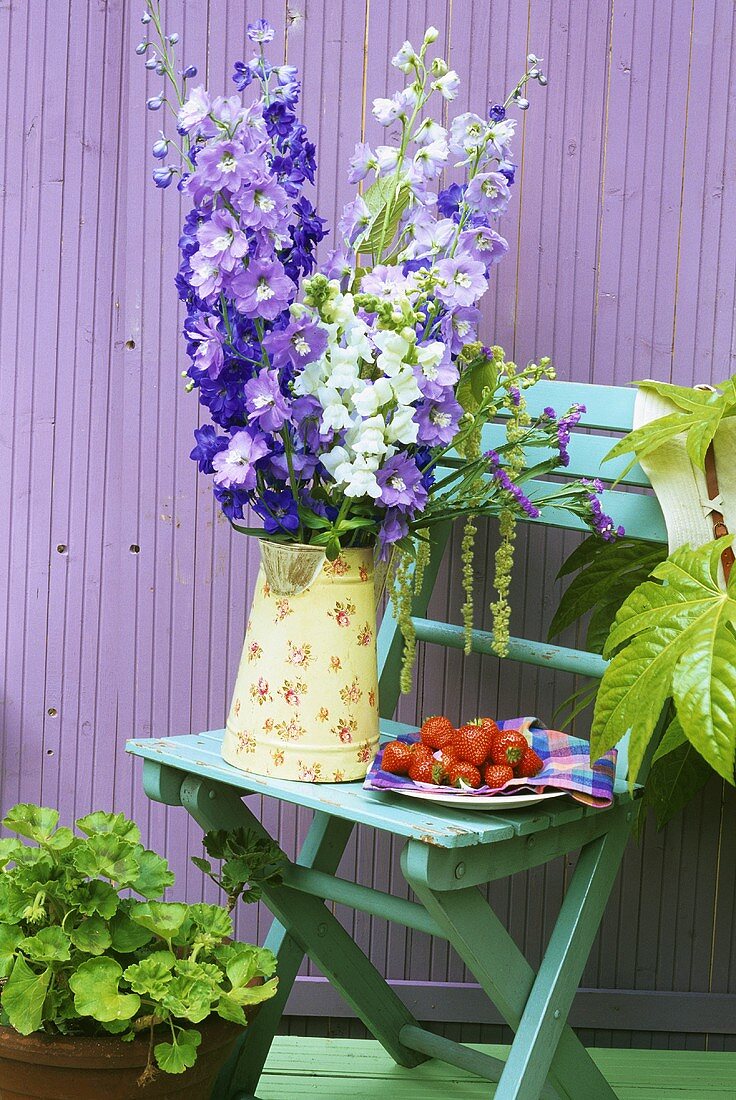 Garden chair with delphiniums and plate of strawberries