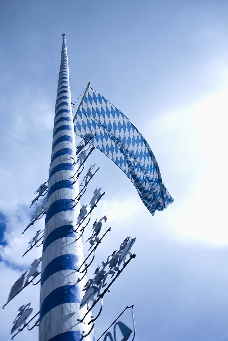 Maypole against blue and white sky with flag (Germany)