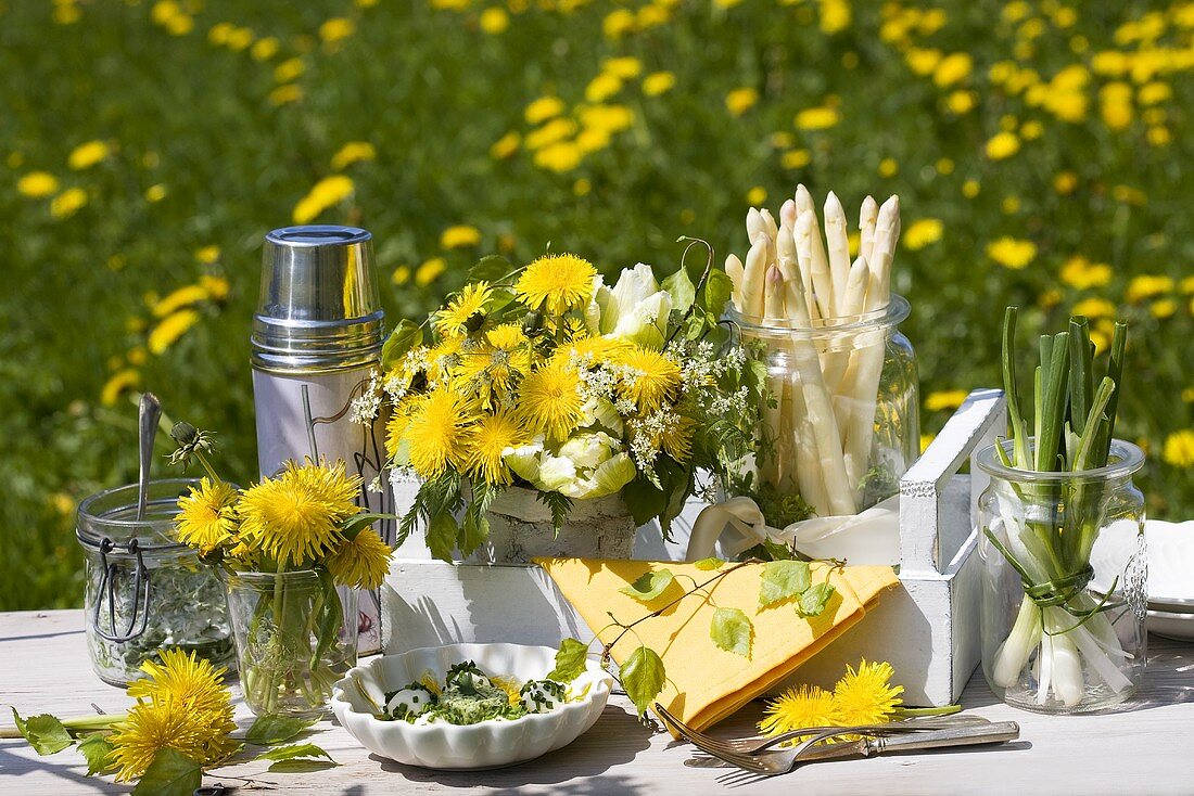 Tisch in Löwenzahnwiese mit Spargel und Frühlingszwiebeln
