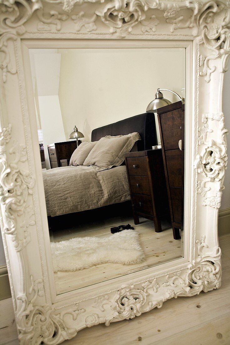 Doppelbett mit Nachtschränkchen spiegeln sich in grossem ornamentalem Schlafzimmerspiegel