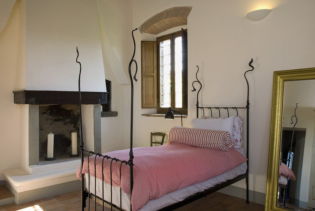 Schmiedeeisernes Bett mit rosa Bettwäsche vor Kamin im Mediterraner Landhaus