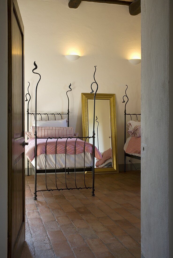 View through an open door into a bedroom with a single bed with a iron bedstead on a tile floor