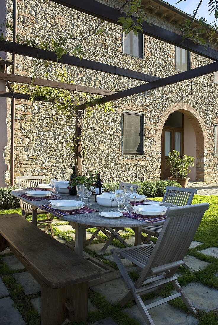 A set table on a terrace in front of a country house with a stone facade
