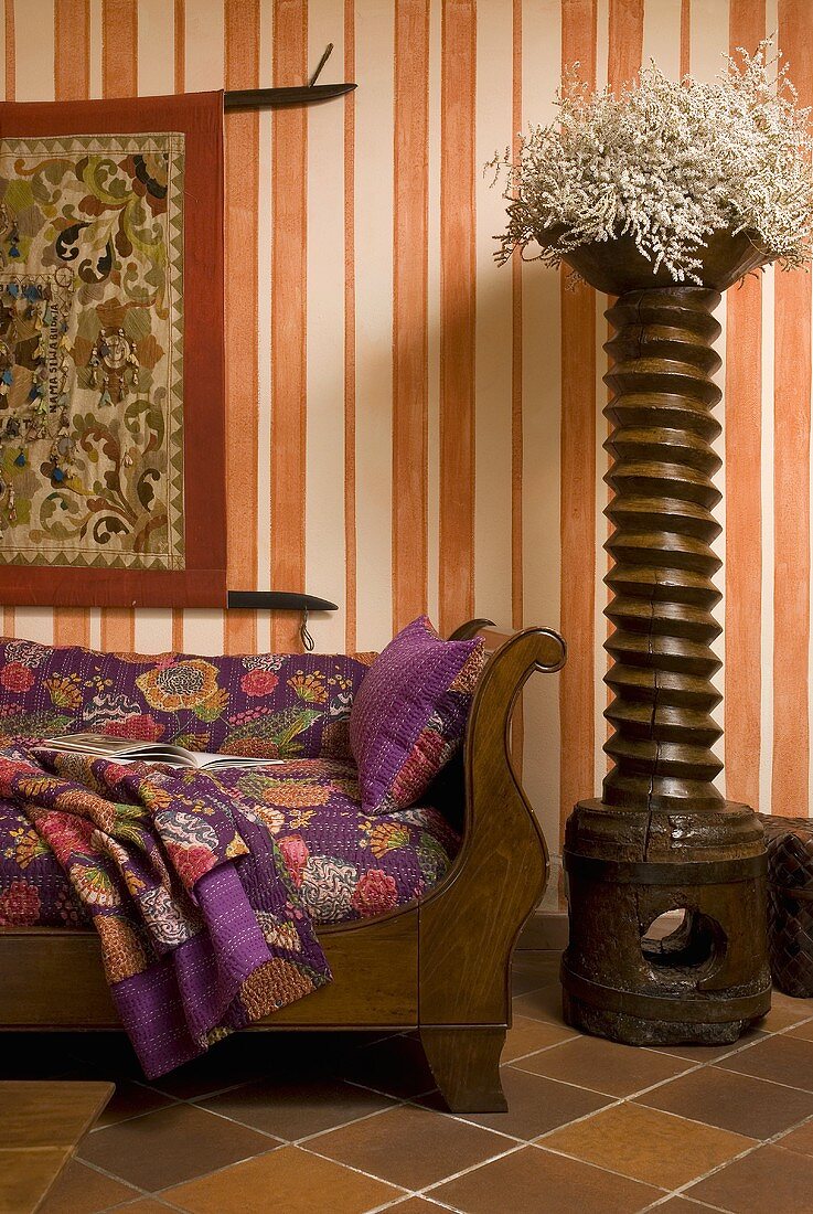 Dekoholzsäule und antike Couch vor Tapete mit orange weißem Streifenmuster