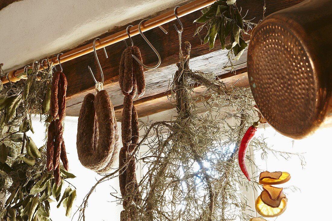 Getrocknete Kräuter und Hartwurstsorten hängen an einer Stange