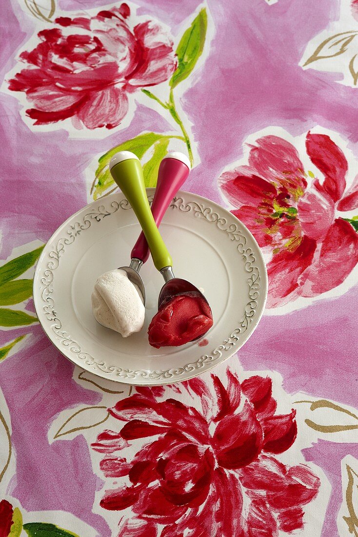 Teller mit Erdbeersorbet und Vanilleeis auf einer sommerlichen Tischdecke mit Blumenmuster