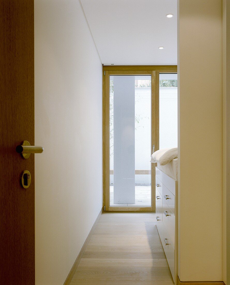 A view through an open door onto a terrace door and a cupboard under a bed